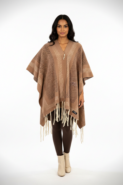 Model wearing a Cozy&Drape brown geometric patterned fringe poncho wrap with a pearl-style clasp over brown leggings.