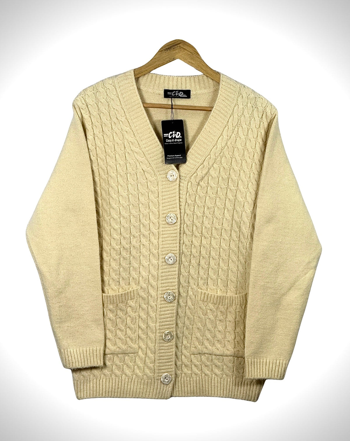 Cozy&Drape cream cable knit cardigan sweater with long sleeves, front buttons, and two pockets on a wooden hanger.