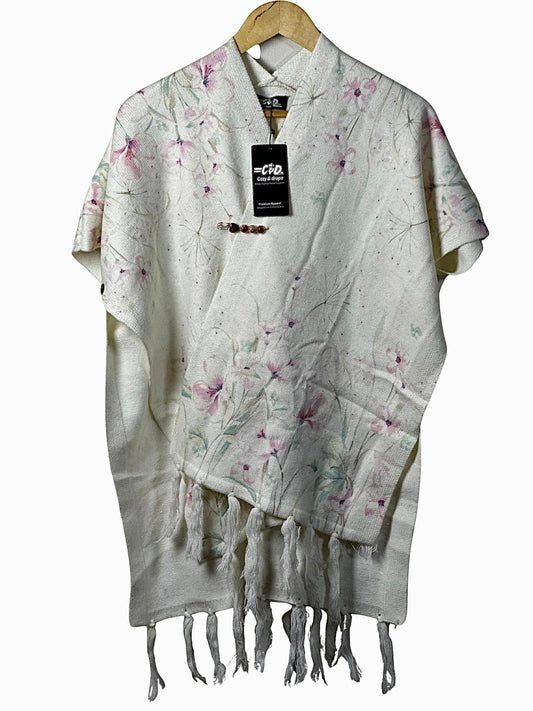 Cozy&Drape cream cape shawl with delicate pink floral print, fringe hem, and decorative brooch on a wooden hanger