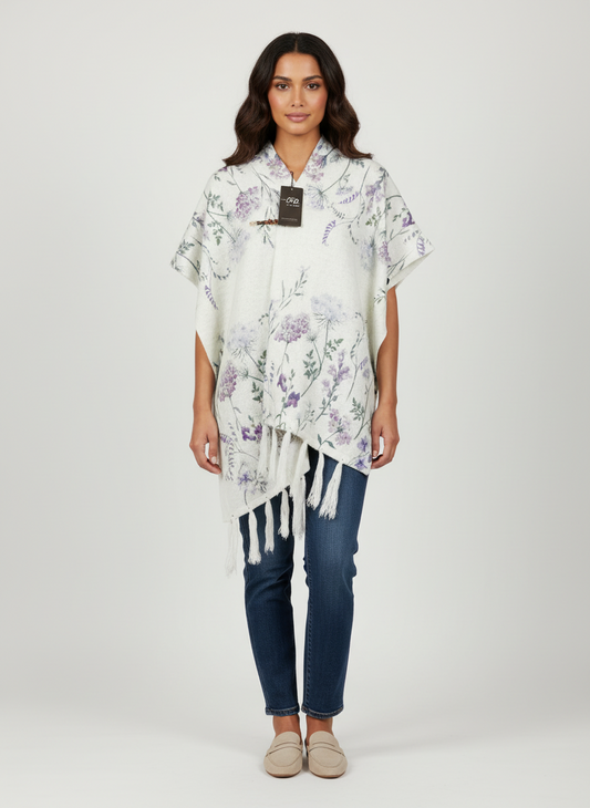 Model wearing a Cozy&Drape white floral print poncho wrap with fringe hem, side buttons, and a decorative clasp.