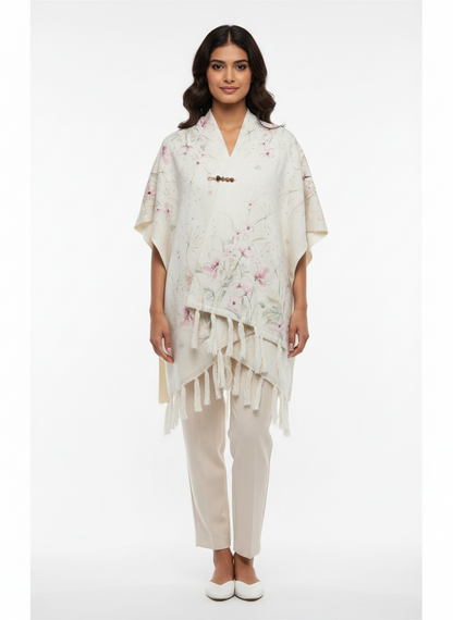Model wearing a Cozy&Drape cream floral print poncho wrap with tassel fringe and a decorative pin on a white background