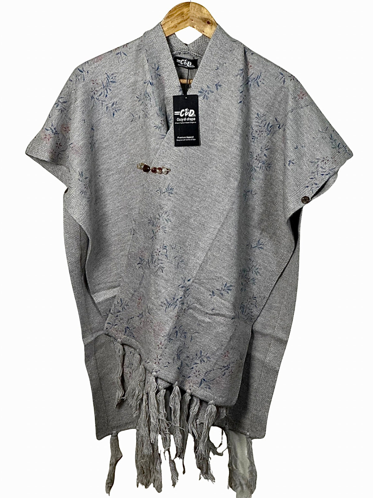 Cozy&Drape grey winter cape shawl with delicate floral print, button detail, and fringe hem on a wooden hanger.