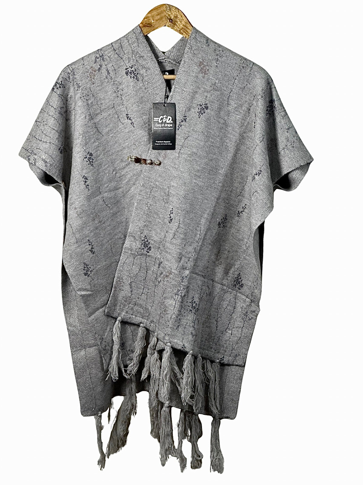 Cozy&Drape grey winter cape shawl with delicate floral patterns, tassel hem, and decorative brooch on a hanger.