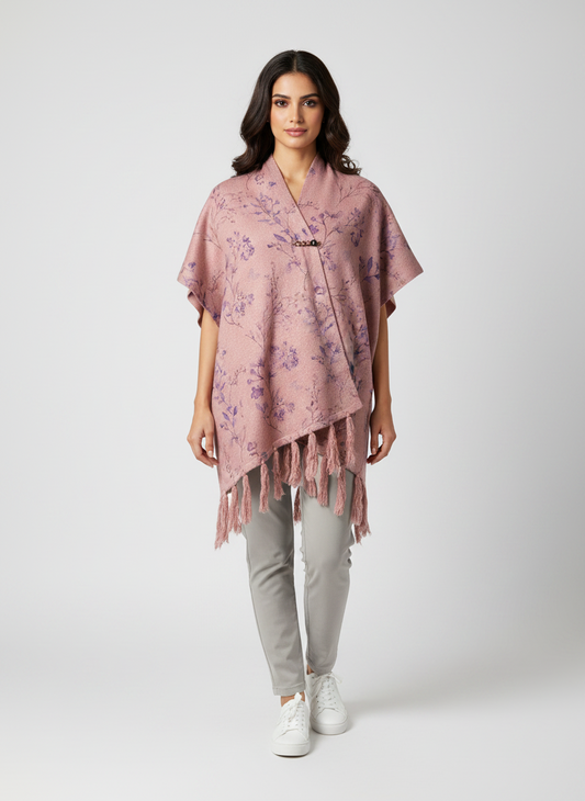 Cozy&Drape mauve floral print cape shawl with fringe hem and toggle closure worn by a woman with grey trousers