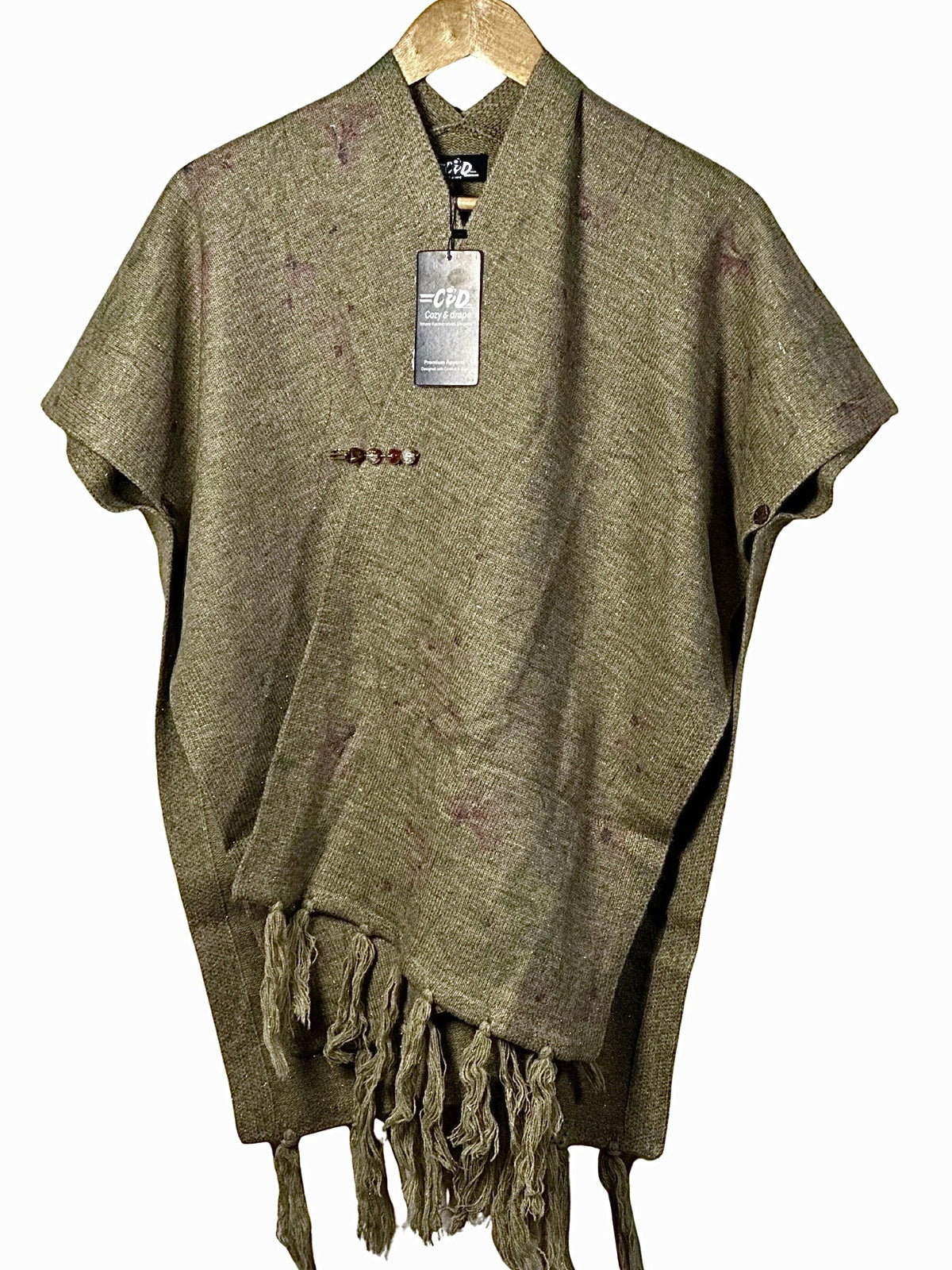 Cozy&Drape olive green winter cape shawl with fringe hem and decorative button detail on a wooden hanger