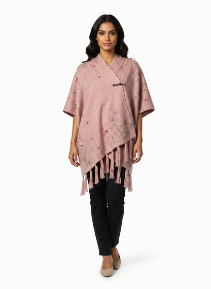 Model wearing a Cozy&Drape pink floral poncho wrap with a decorative brooch closure and tassel hem details.