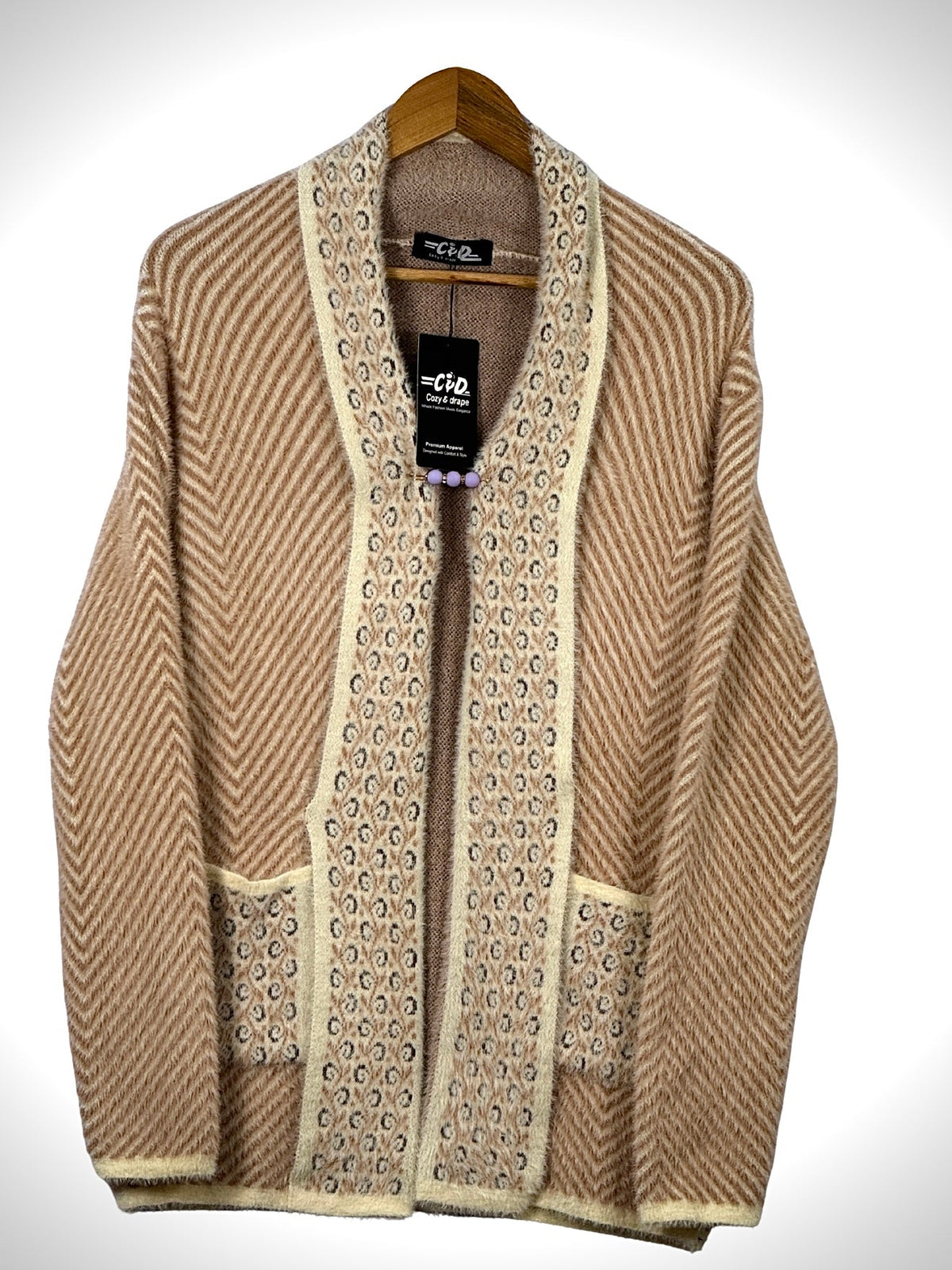 Cozy&Drape open front sweater in tan with chevron pattern, cream trim, and front pockets on a wooden hanger.