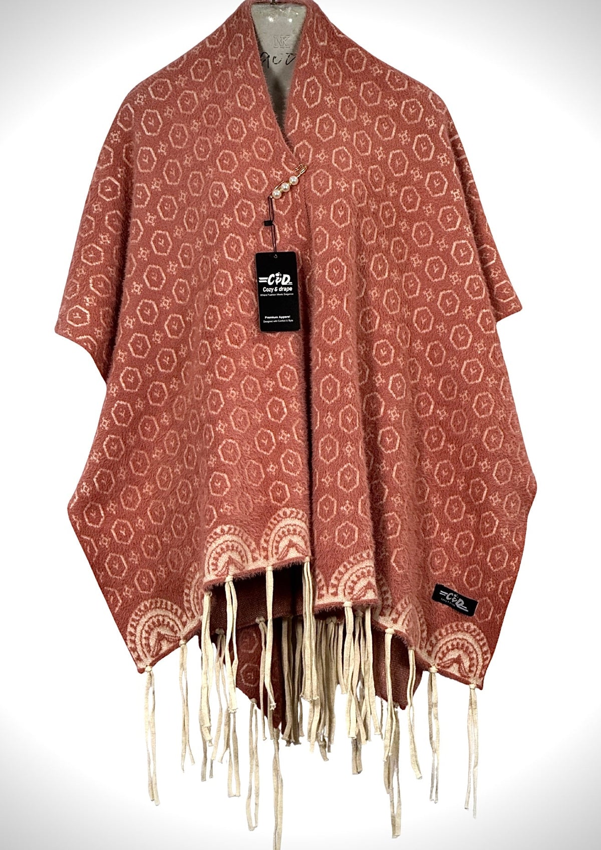 Cozy&Drape terracotta winter cape shawl with geometric hexagon pattern, fringe hem, and elegant pearl pin closure.